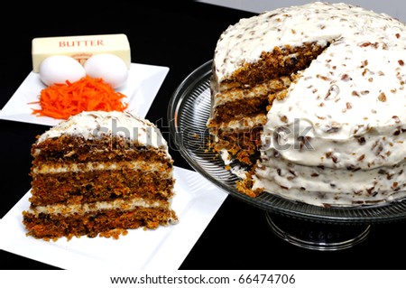Slice of carrot cake on white plate with whole cake and ingredients in background.