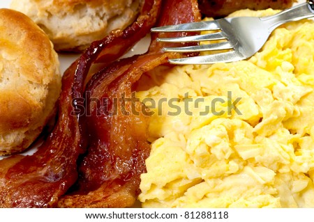 Closeup of scrambled eggs, bacon slices, biscuits, and fork