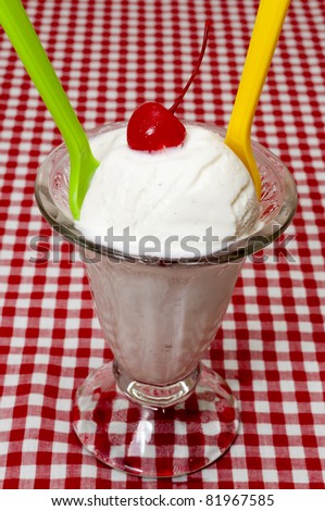 Vanilla ice cream and spoons with cherry topping on table with red gingham table cloth.