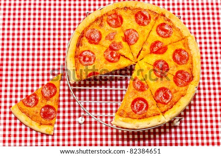 Whole pepperoni pizza on rack with slice removed.  Red gingham tablecloth.