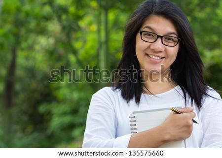 Happy female student in the park, holding notebook and smiling