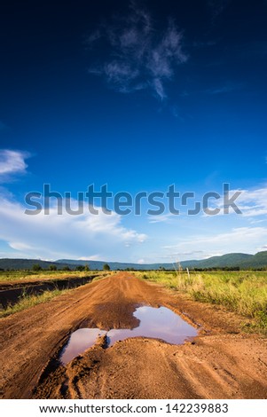 Soil road with muddy tracks under blue sky