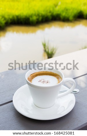 Coffee on wood bench with green rice field