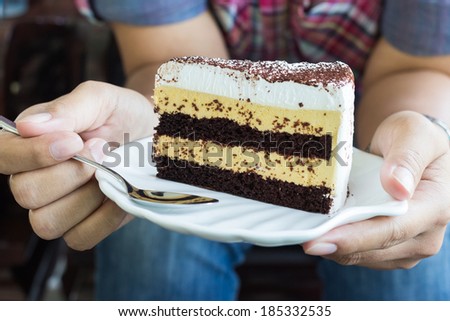 Closeup woman\'s hand holding butter and chocolate cake in white plate