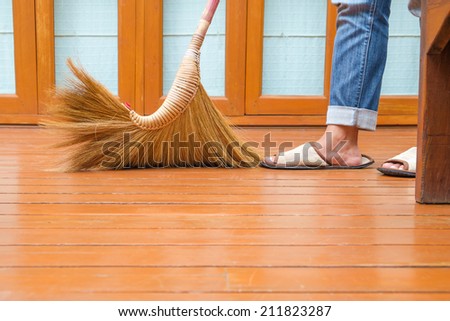 Sweeping dust on wood floor, closeup  at broomstick with woman's feet in slippers