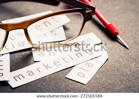 Marketing plan word printed on pieces of paper with eyeglasses and dart