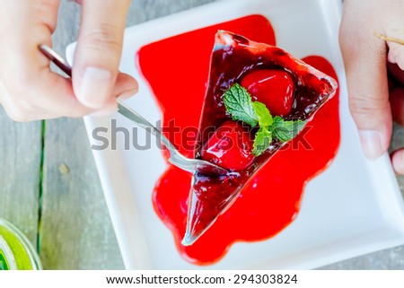 Crape cake with strawberry sauce on white plate, with woman\'s hand going to serve