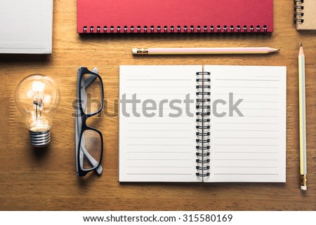 Tools for writing, Many notebooks with pencils and glowing light bulb on wood table