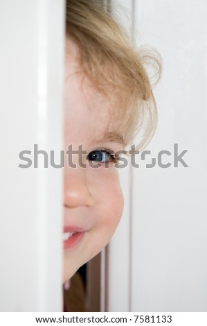 Smiling young girl behind a door. Focus is on the eye