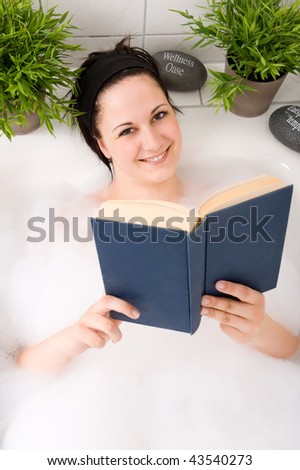 Young and beautiful woman reading a book in the bathtub