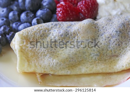 A blueberry crepe covered with maple syrup accompanied with blueberries and raspberries