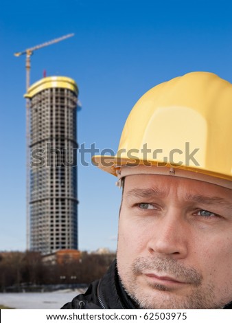 Face builder in the yellow helmet on the background of high-rise building under construction