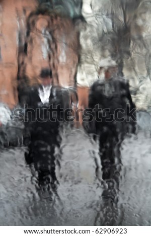 Views of the silhouettes of two men walking in the rain through wet glass
