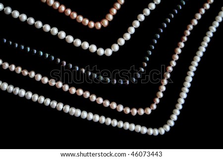 White, black and pink pearls on the black silk as background