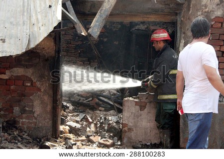 LAHORE, PAKISTAN - JUN 17: Fire fighters extinguishing from burning goods while residents gather at the site after fire broken out incident at LPG Gas Shop on Wehdat road on June 17, 2015 in Lahore.