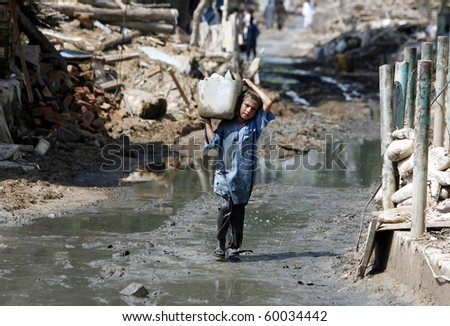 NOWSHERA, PAKISTAN - AUG 29: A child carries household items while passing through the rubble of houses on August 29, 2010 in Nowshera. The homes were destroyed by flood waters.