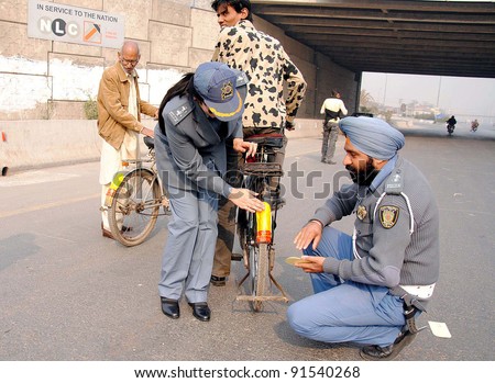 LAHORE, PAKISTAN - DEC 27: Traffic wardens paste reflective stickers on bicycles during a campaign at Ravi River underpass in Lahore on Tuesday, December 27, 2011.