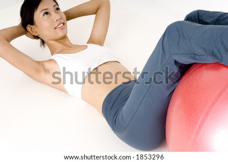 A pretty young asian woman doing sit-ups with a fitness ball to assist