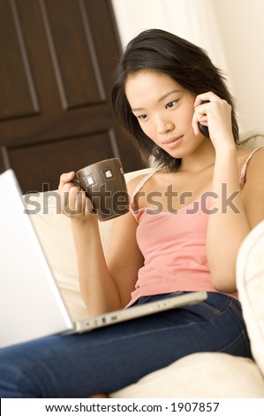 An attractive young woman sitting on a sofa with laptop, phone and mug of drink (shallow depth of field used)