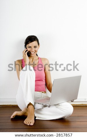 A young woman on mobile phone sitting with laptop computer on wooden floor
