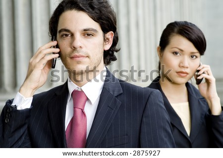 A young man and woman in business attire holding mobile phones outdoors