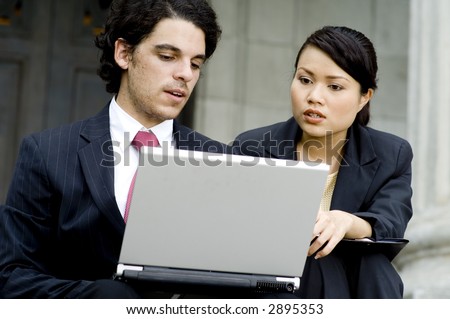 A young businessman and businesswoman working on a laptop computer outside