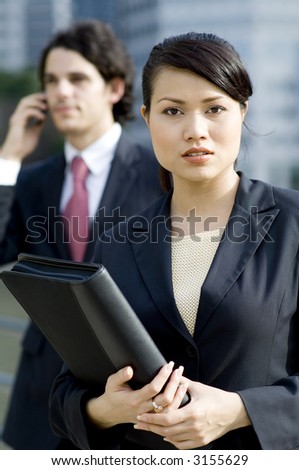 A young asian businesswoman holding document folder with male colleague standing behind (shallow depth of field used)