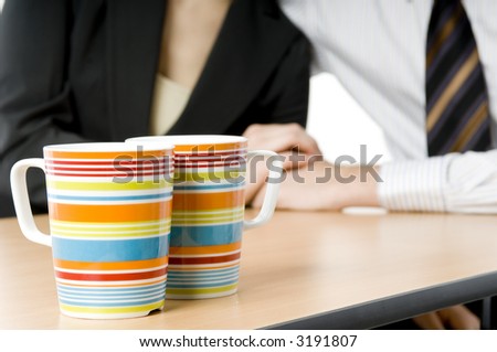 A pair of colorful coffee cups (in focus) with two business people holding hands in background
