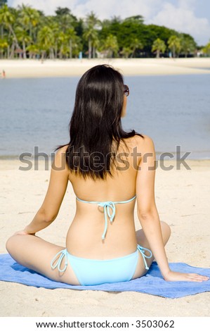 A young asian woman in blue bikini sitting on a sunny beach