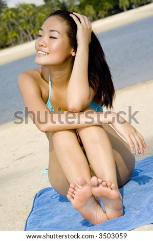 A young attractive asian woman in blue bikini sitting on a tropical beach