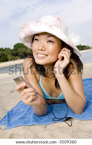 A young attractive woman relaxing on the beach with a digital music player