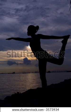 A young woman doing yoga by the ocean at sunset