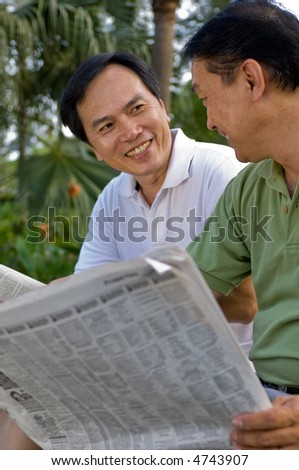 Two Chinese men in their fifties reading the newspaper in the park