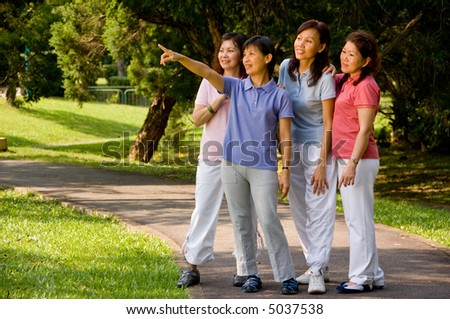 A group of Asian women standing together in the park looking at something of interest