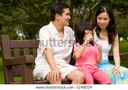 A young couple with a small child spending time together blowing bubbles on a park bench