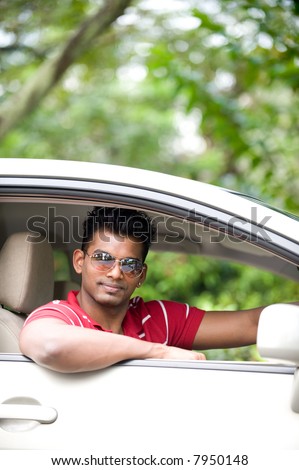 A good-looking Indian man in sunglasses sitting in drivers seat of car outside
