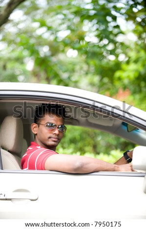 A good-looking Indian man in sunglasses sitting in drivers seat of car outside