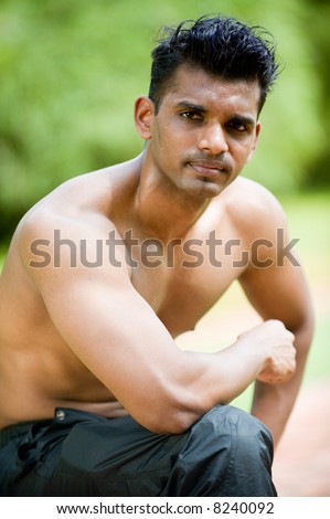 A young man with no top on kneeling down outside