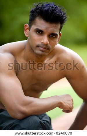 A young man with no top on kneeling down outside