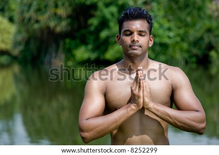 A well-built Asian man practicing yoga outside by water