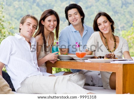 A group of four young adults sitting together to enjoy a meal with drinks outdoors