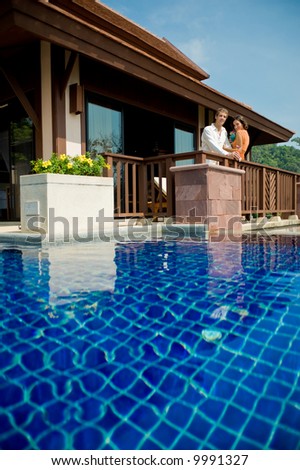 A young attractive couple standing by their pool villa with drinks