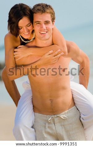 A good-looking young man gives his partner a piggy-back on the beach
