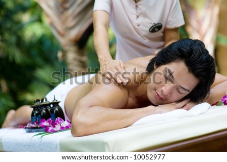 A young man getting a massage outside at a tropical spa