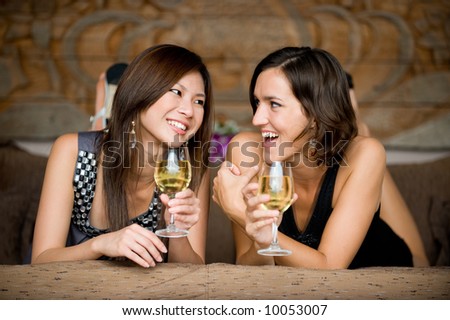 Two young attractive women with wine lying on bed
