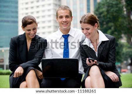 Two businesswomen and a businessman outside with laptop and phone
