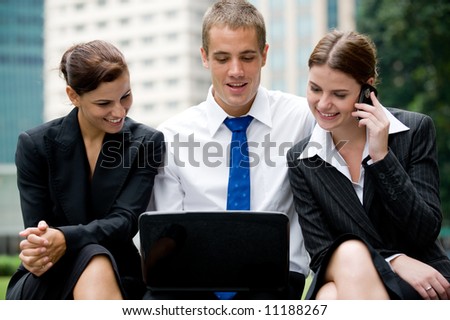Two businesswomen and a businessman outside with laptop and phone