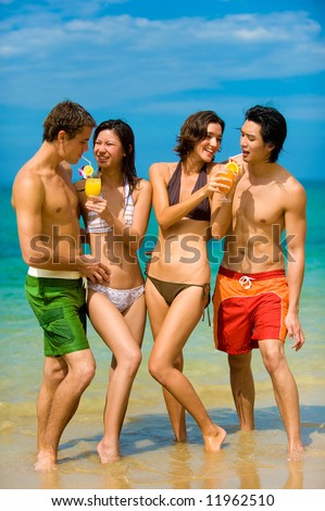 Four young adults standing by ocean with drinks