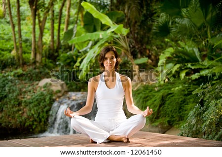 A young woman sitting outside in a yoga position looking very peaceful