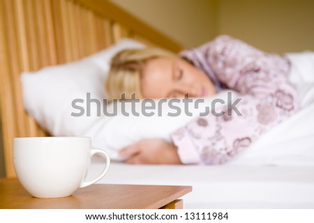 A young woman in pyjamas in bed reaching for morning coffee